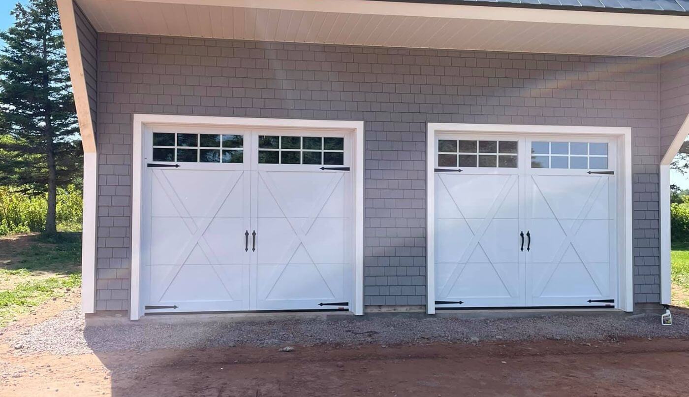 Two white garage doors featuring windows, positioned beside a residential house.
