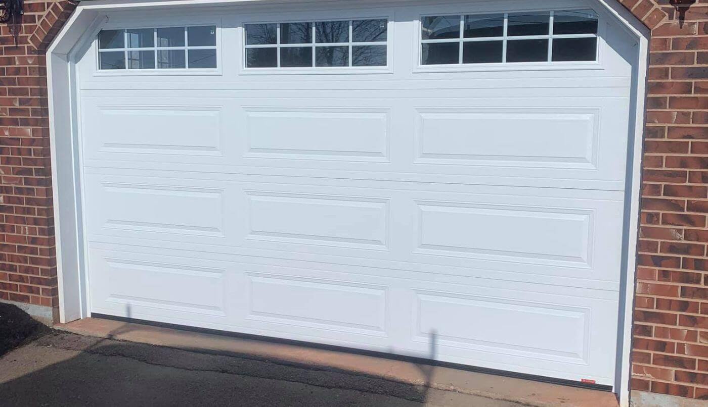 A white garage door set against a textured brick wall, showcasing a clean and classic architectural design.