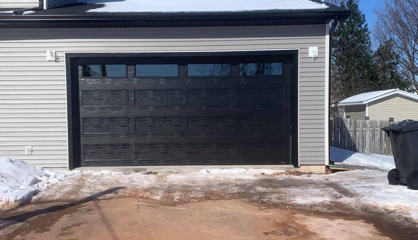 A garage door featuring a black frame, set against a snow-covered driveway, creating a serene winter scene.